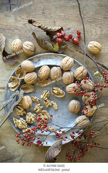 Whole and cracked organic walnuts, roseships and nutcracker on tin plate