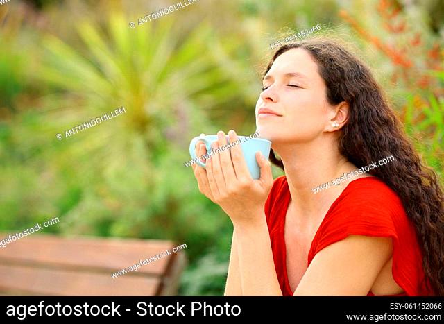 Relaxed woman smelling coffee in a green park