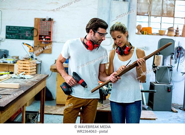 Male and female carpenters checking wooden plank