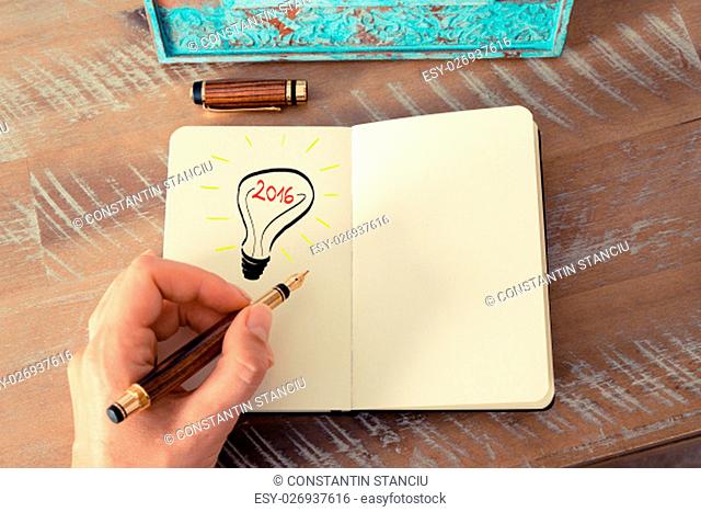 Retro effect and toned image of a woman drawing a lighting bulb with fountain pen on a notebook. Year 2016 symbol for bright idea and business concept