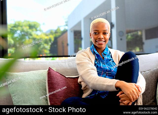 Portrait of happy african american woman sitting on sofa, looking at camera and smiling