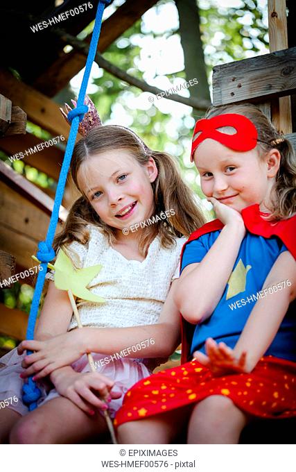 Girls dressed up as princess and superwoman playing in a tree house