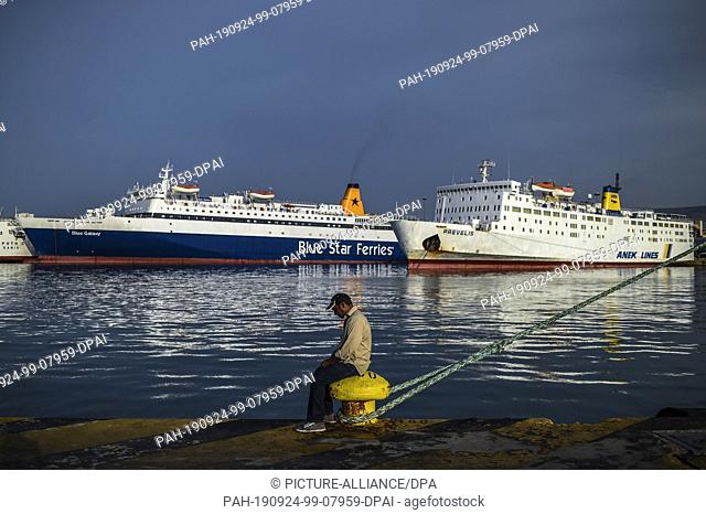 dpatop - 24 September 2019, Greece: During a 24-hour strike in the port of Piraeus, a man sits on a berth in front of the docked ferries