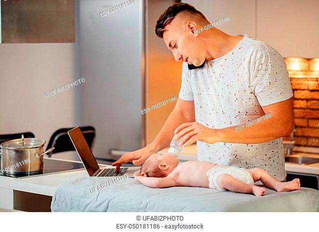 Multitasking Father Feeding His Baby While trying Working on laptop and cooking