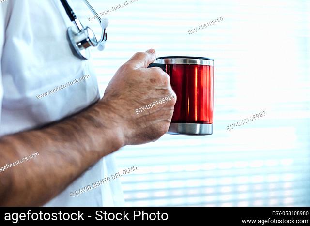 Mature male doctor - nurse having coffee in a hospital window. Covid-19 and medicine concept