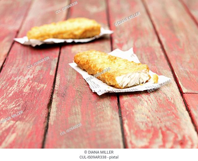 Two fried chunky battered cod pieces on red wooden table