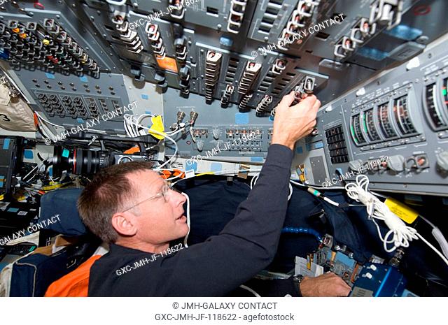 NASA astronaut Chris Ferguson, STS-135 mission commander, toggles switches on the overhead panel of the forward flight deck of the space shuttle Atlantis