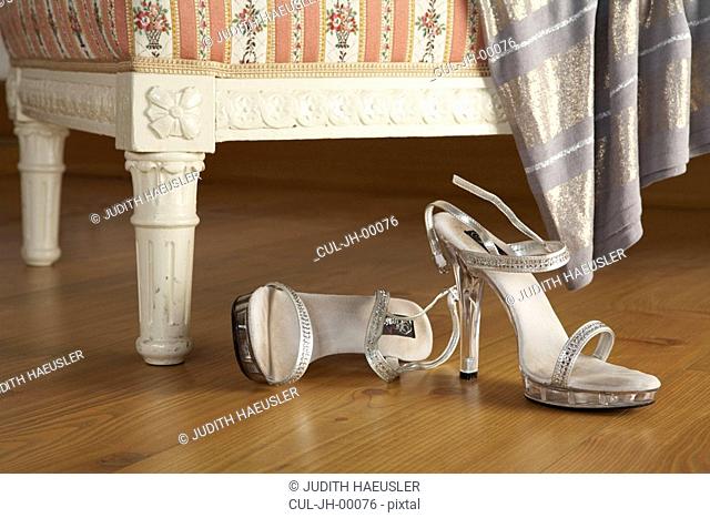 two silver high-heeled womans sandals on wooden floor, close-up