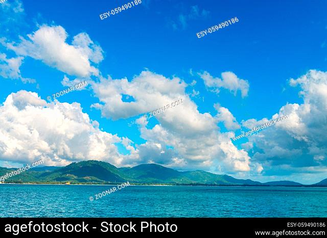 Sunny day with blue cloudy sky at tropical island coast. View from the sea