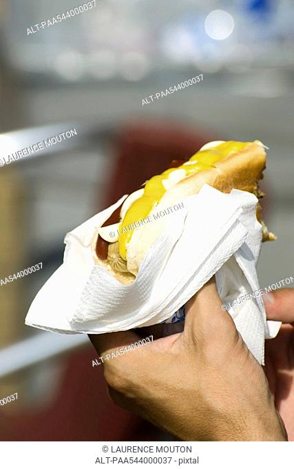 Hand holding hotdog in bun with ketchup and mustard