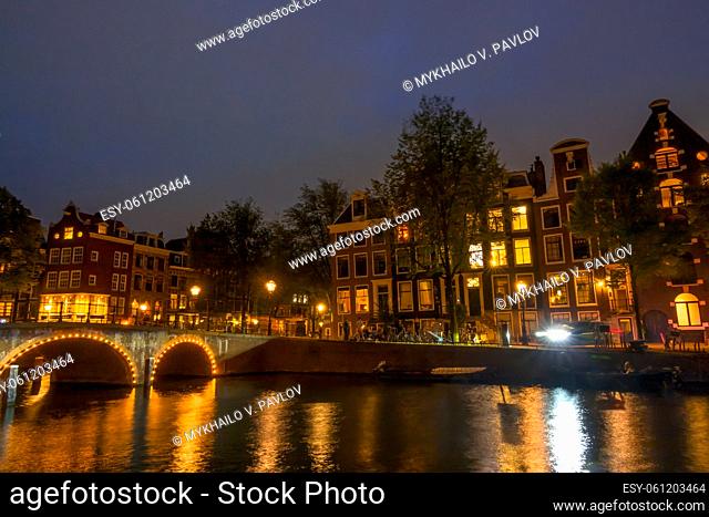Netherlands. Night on the Amsterdam canal. Old stone bridge and typical houses on the embankment. Traffic on the water and streets