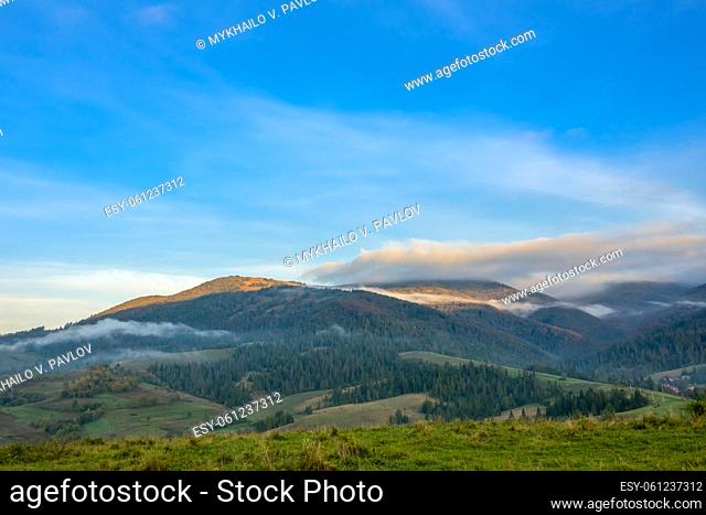 Summer Ukrainian Carpathians and sunny morning. Light mist between wooded mountains. The first rays of the sun illuminate the mountain peaks
