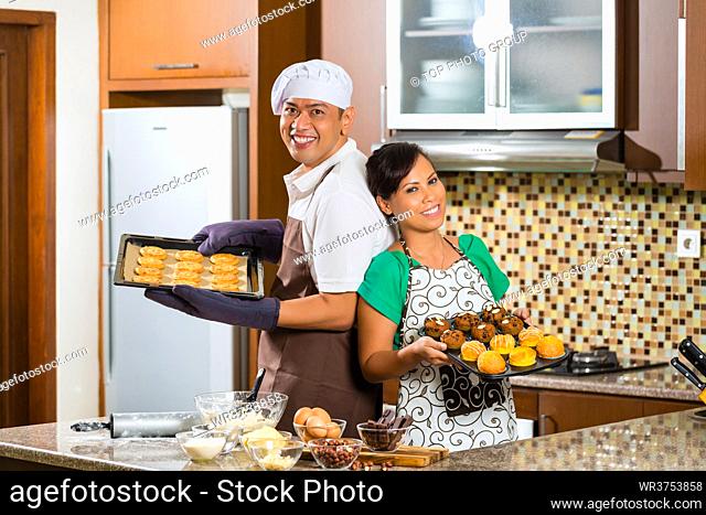 Asian couple, man and woman, presenting homemade cup cake muffins they bake in their kitchen for dessert