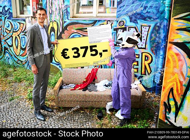 09 August 2021, Berlin: Neukölln's district mayor Martin Hikel (l, SPD), together with the district mascot, holds an oversized price tag over a couch that was...