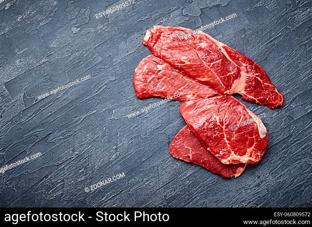 Four raw ribeye steak on a black background. View from above