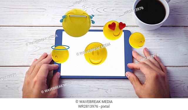 Digitally generated image of various emojis flying over hand using digital tablet at wooden table