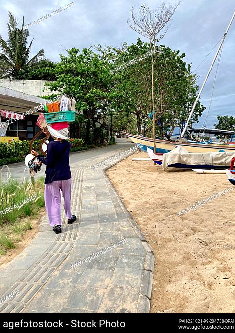 19 October 2022, Indonesia, Sanur: A beach vendor walks along the empty boardwalk on the beach. On the Indonesian vacation island of Bali