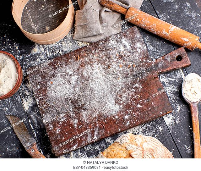 bread, white wheat flour, wooden rolling pin and old cutting board on a black table, top view