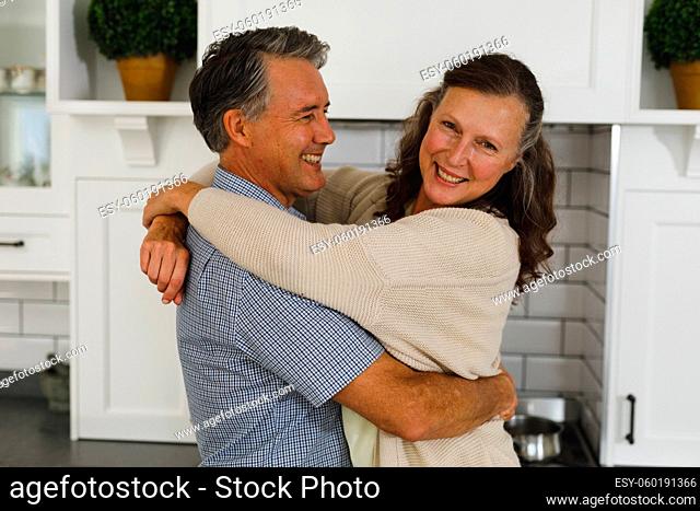 Happy senior caucasian couple in modern kitchen, embracing and smiling