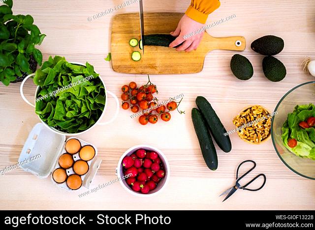 Woman chopping cucumber on cutting board at kitchen
