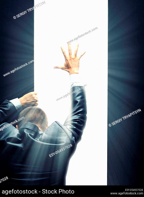 Businessman opening some gate and reaching hand to a bright light