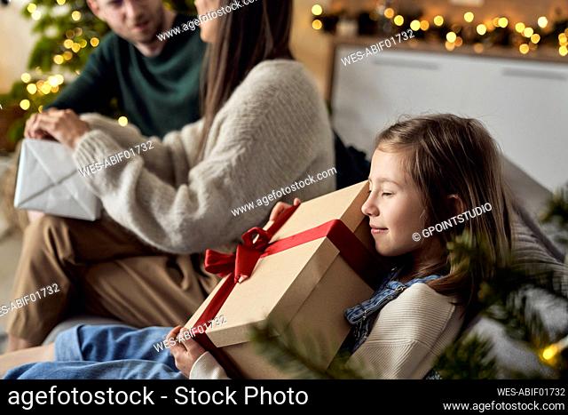 Smiling girl embracing gift box sitting by parents at home