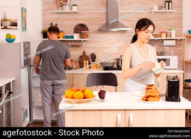 Housewife in pajamas preparing breakfast making roasted bread on electric toaster. Young couple in the morning preparing meal together with affection and love
