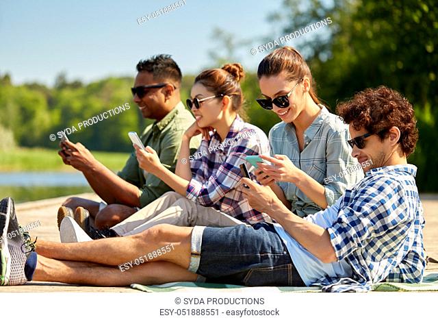 friends with smartphone on lake pier in summer