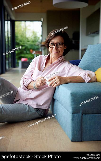 Smiling senior woman leaning on sofa with coffee cup at home