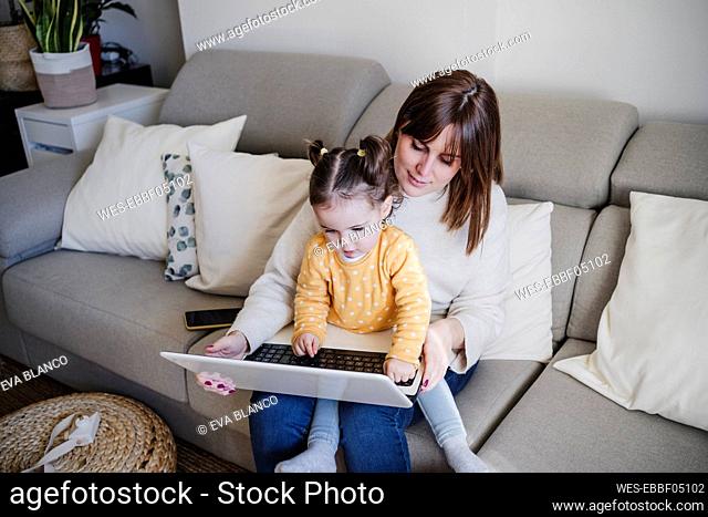 Mother using laptop with daughter on sofa