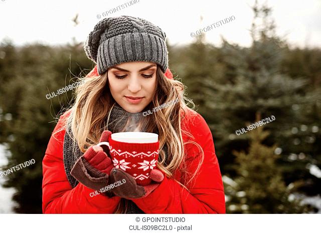 Portrait of young woman with coffee in christmas tree forest