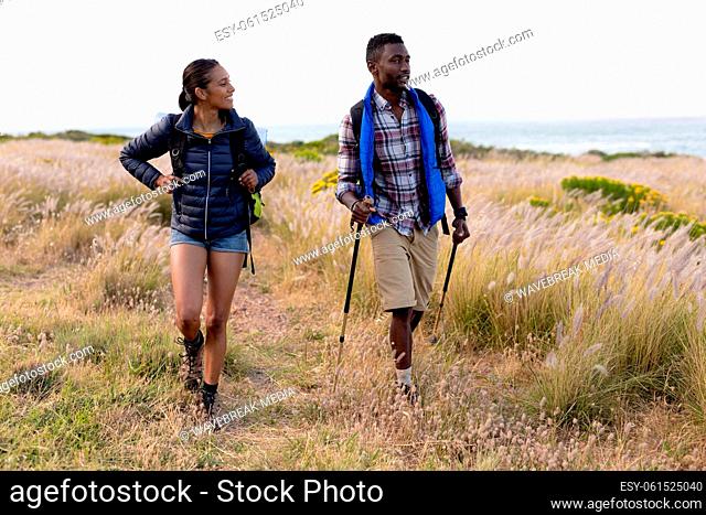 Fit african american couple wearing backpacks hiking in coastal countryside