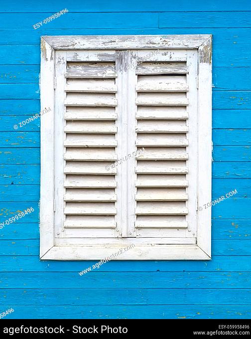 Old white window with wooden shutters on the blue wall of boards