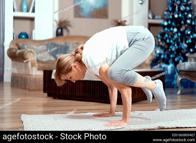 Strong Mature Woman Balances On Her Arms While Lifting Her Legs. Concentrated Woman Practices Yoga Pose Standing On Arms. Balance