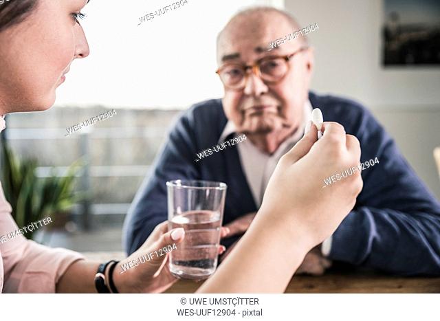 Woman holding pill and glass of water for senior man