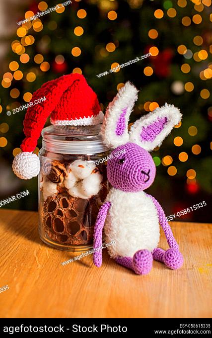The knitted toy rabbit in purple color on a wooden stand near with dried flowers in a jar. Home decor concept for christmas