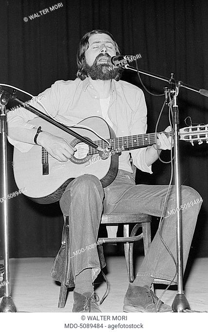 Italian singer and writer Francesco Guccini sitting with a guitar and a mic while performing on stage at Teatro Quartiere in Quarto Oggiaro