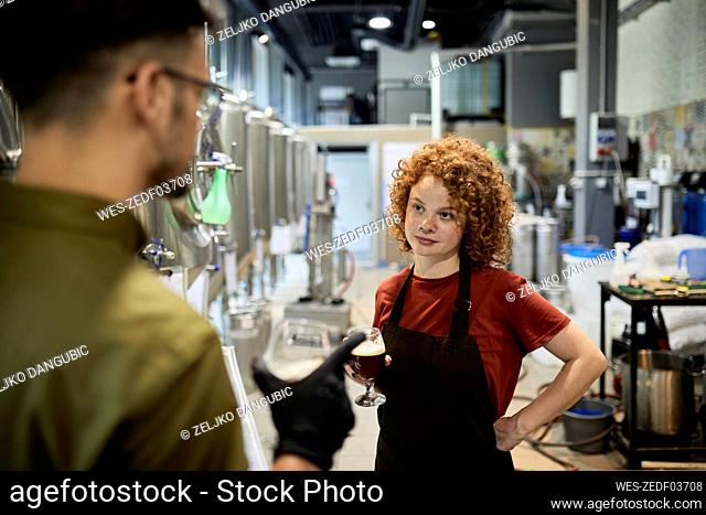 Man and woman working in craft brewery checking quality of a beer