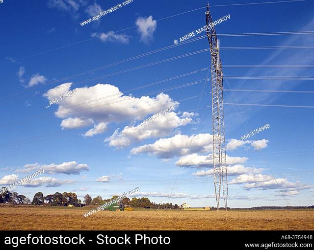 A power line across the oat field with a combine and white clouds in the blue sky. Hinterland. Sweden