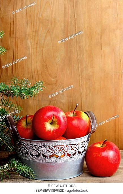 Silver bucket of red apples on wooden table. Copy space