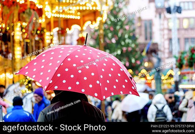 21 December 2023, Hesse, Frankfurt/Main: A man stands with an umbrella at the Christmas market in the banking city. According to the forecast by the German...