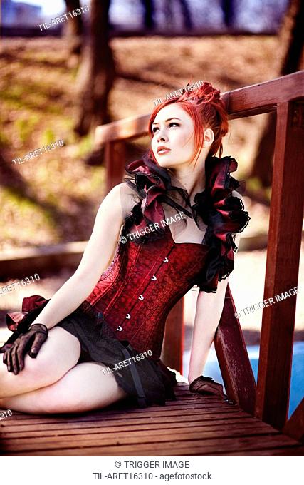 Redhead dressed in Victorian style sitting on a wooden bridge