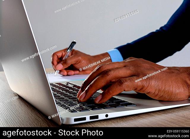 Close up of businessman using laptop and taking notes against grey background