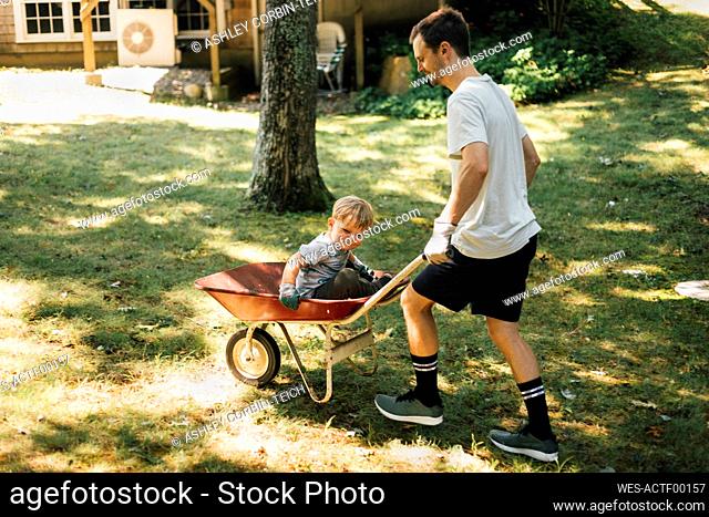Father pushing son sitting on wheelbarrow