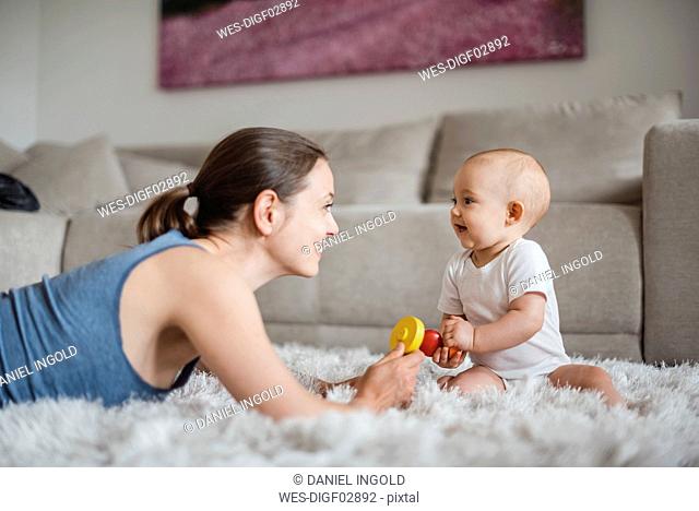 Happy baby girl with mother playing on carpet at home