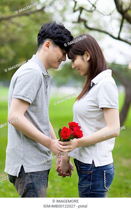Young couple holding flowers and looking down with head to head