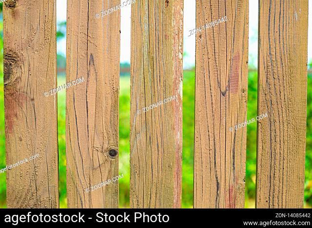light beige wooden fence with gaps, vertical boards on a green field