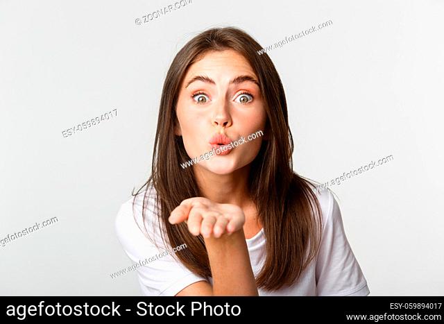 Close-up of beautiful flirty girl pouting lips and sending air kiss at camera
