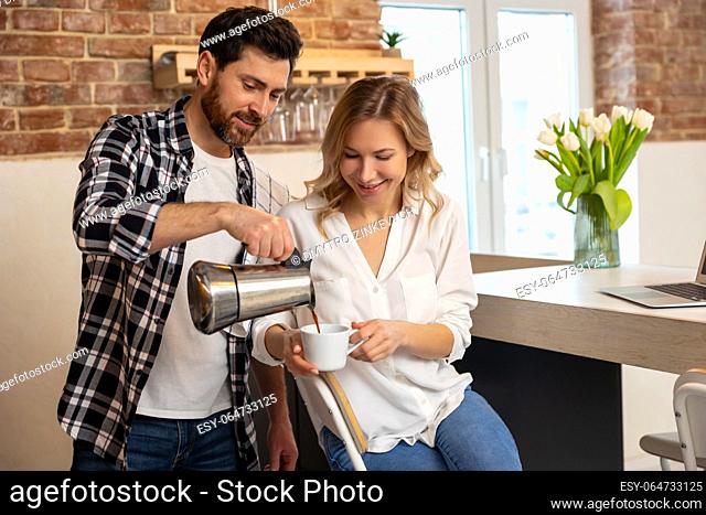 Young man serving coffee to his girlfriend having breakfast in kitchenn at home