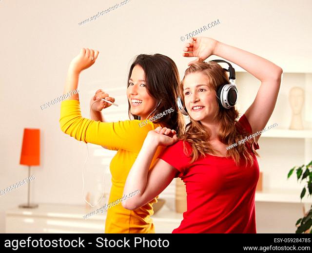 Happy teen girls listening to music having fun together at home dancing smiling